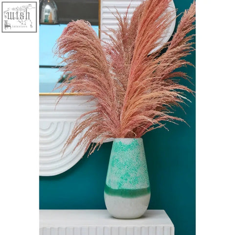 A teal and white ceramic vase with pink pampas grass beside a mango wood wall mirror with a white finish