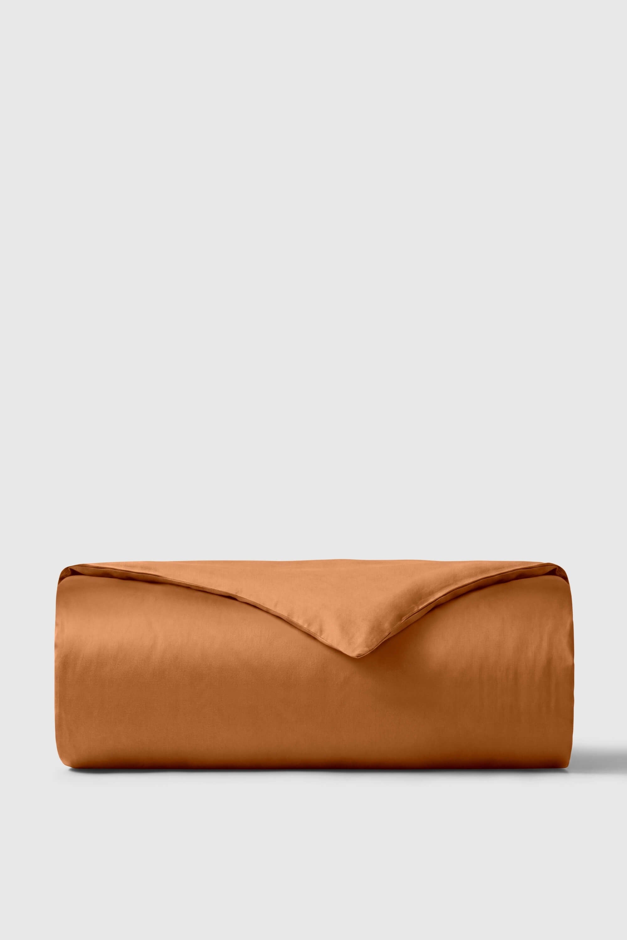 A smooth rust-colored sateen duvet cover neatly folded into a cylinder showing soft satin texture