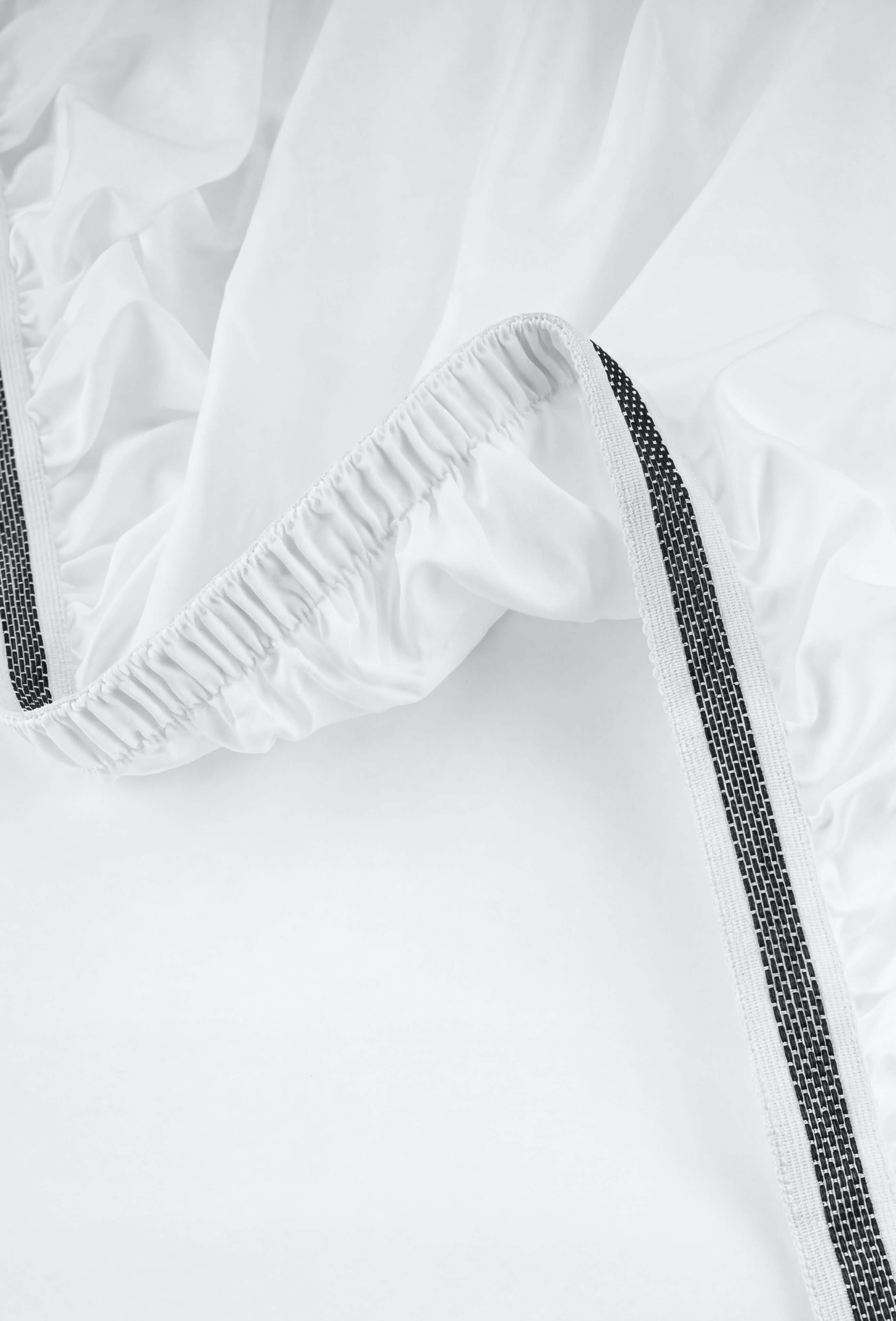 White elasticated sateen essentials bedding fabric with a black textured stripe along the edge in essentials bedding set