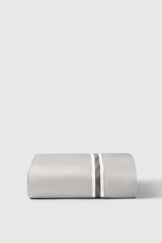 A neatly folded gray linen duvet cover with a white and textured black stripe shown with the sateen fitted sheet