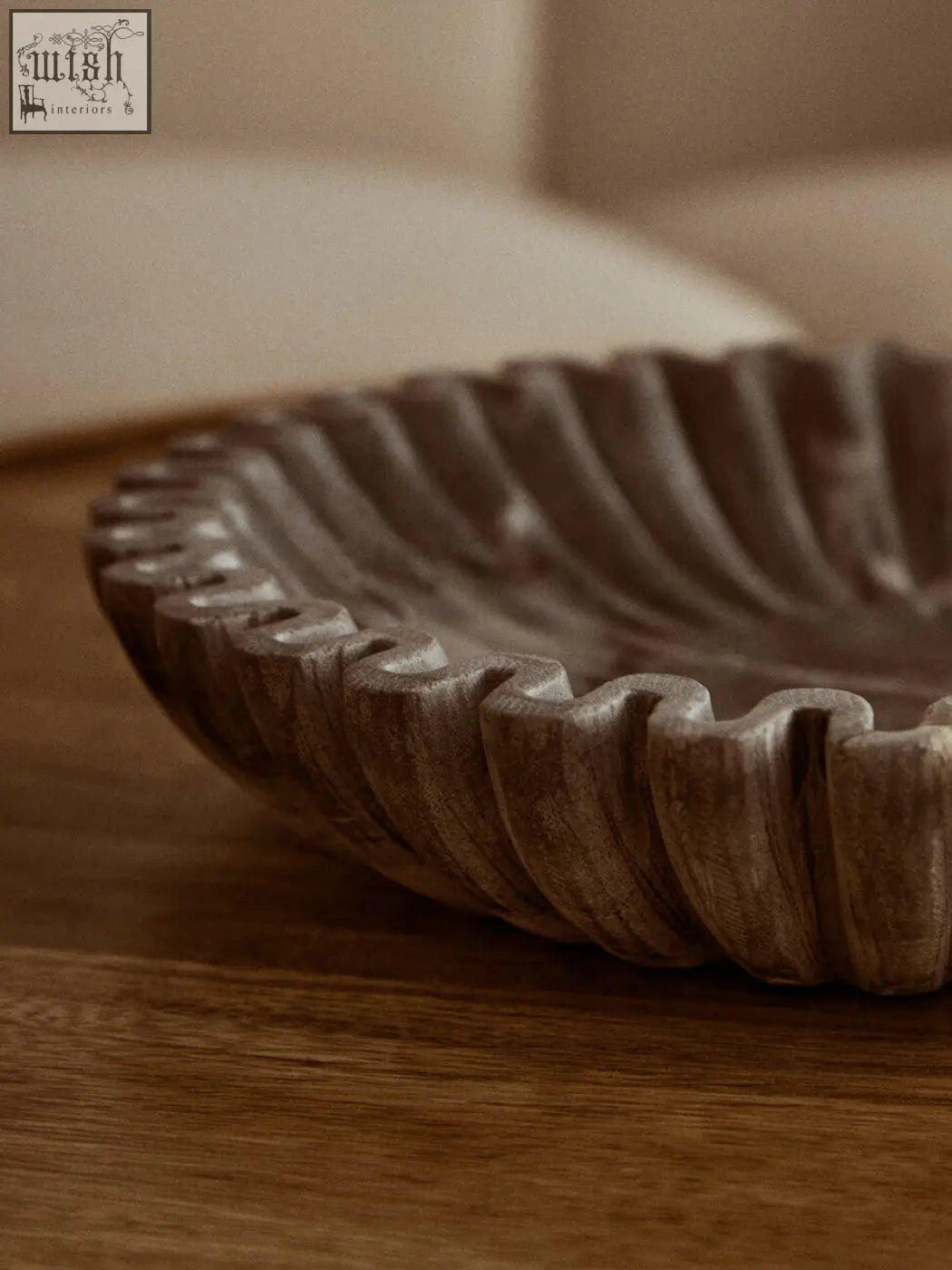 A rustic light brown wooden serving dish with scalloped edge and ridges alongside a grey fluted marble bowl for compact surfaces