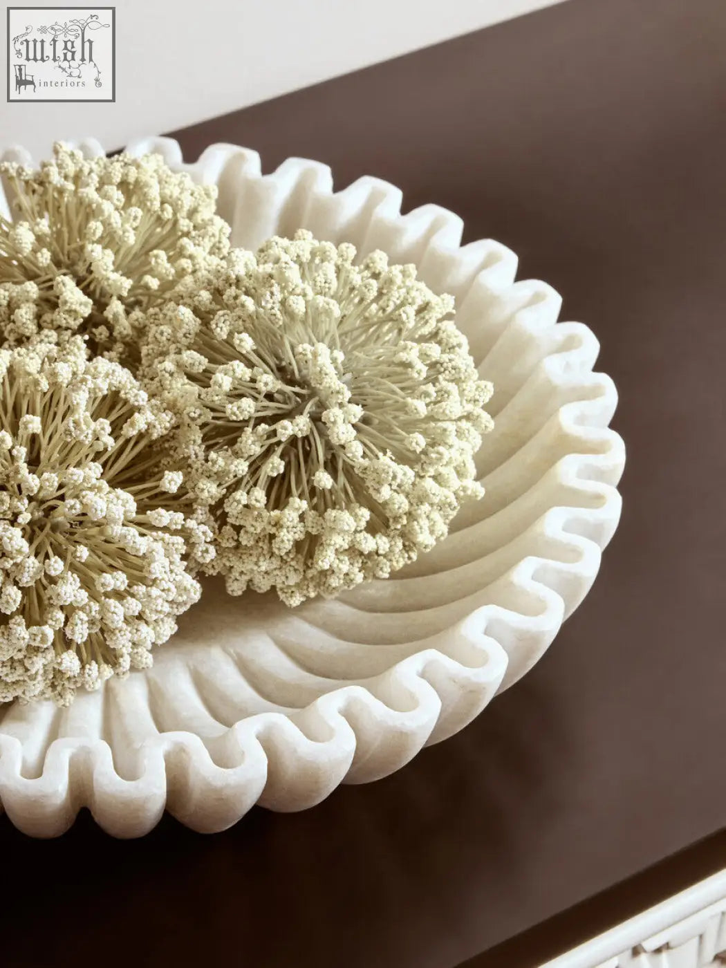 White marble bowl with scalloped edges holding dried cream-colored spherical flowers in the savio large white fluted marble bowl