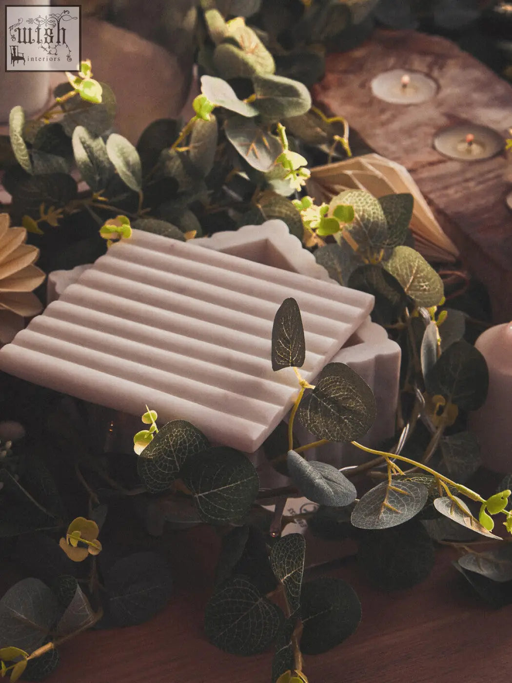 A pale pink ribbed soap bar with a glossy finish sitting in a savio square white fluted marble box with green foliage