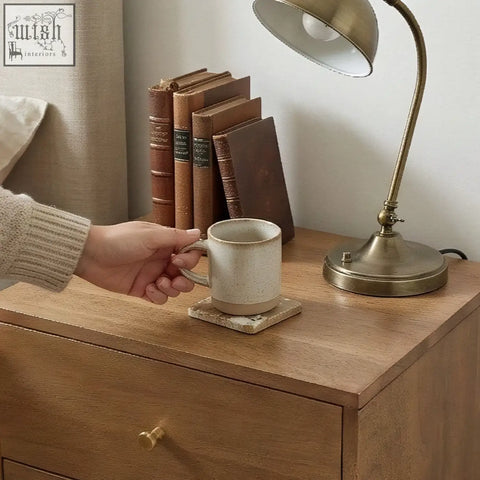 Beige speckled ceramic mug with simple handle on matching stone coaster on scandinavian light walnut oslo bedside table