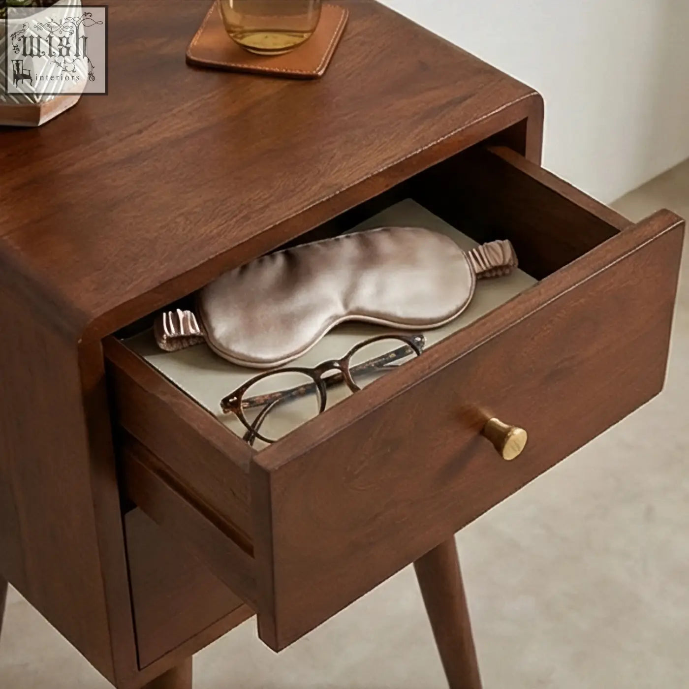 A soft metallic rose gold satin sleep mask resting inside a scandinavian walnut logan narrow bedside table drawer measures 30cm wide