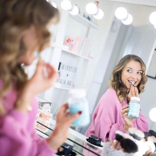 A woman in a pink sweater holding a light blue jar in front of a scarlett large hollywood mirror 100x70cm
