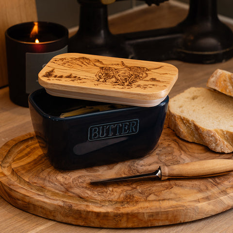 Dark blue ceramic butter dish with light wood lid engraved with scenic highland cow and mountain landscape