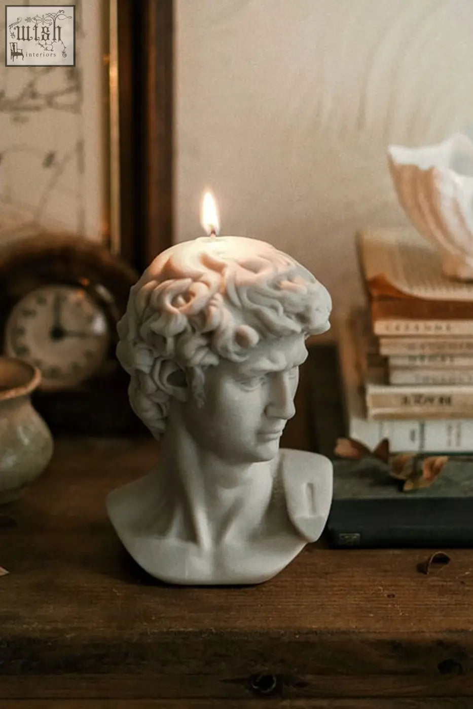 A lit white scented david bust candle shaped like a classical bust with detailed curly hair and sculpted features