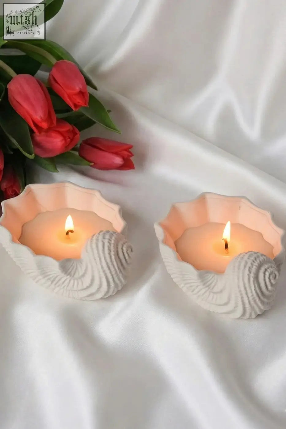 Two pink and white seashell shaped candles with ylang ylang scent lit inside seashell shaped holders