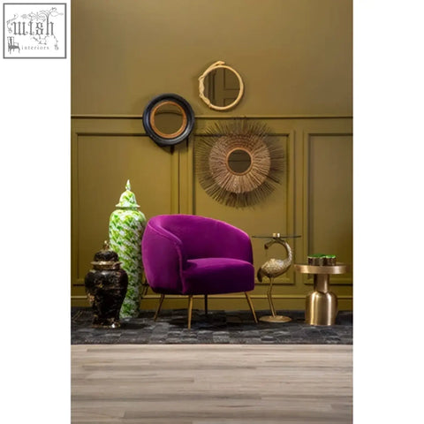 Vibrant purple velvet armchair with gold tone metal legs next to a dramatic texture serpent wall mirror