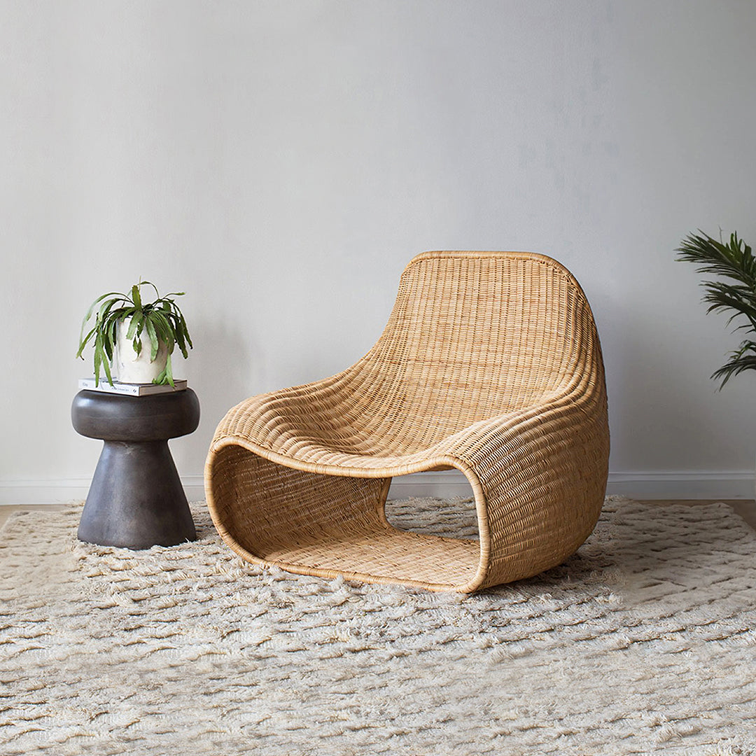 A sleek tan rattan lounge chair with modern curved design and open seating perfect for outdoor use