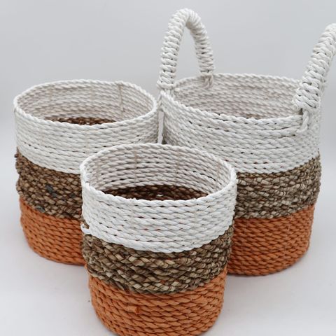 Set of 3 orange seagrass storage baskets with white beige and coral stripes and braided handles on bathroom counter