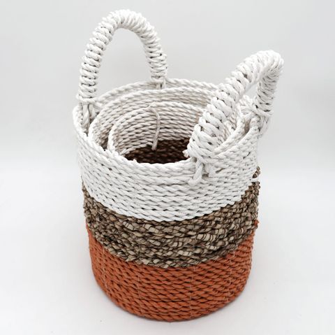 A woven orange seagrass storage basket with two white handles in layered white beige and terracotta tones for organizing