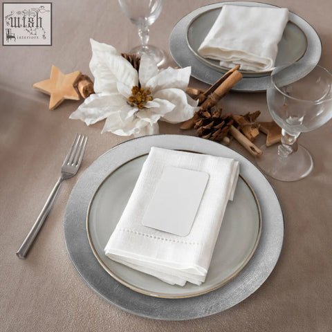 White linen napkin with subtle embroidered edge on silver charger plates with distressed finish to protect table surfaces