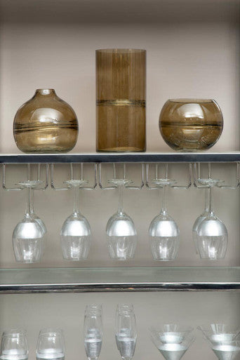 Three amber glass vases with metallic bands on a shelf above hanging apollo large wine glasses set of four
