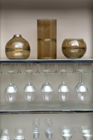 Three amber glass vases with metallic bands on a shelf above hanging apollo large wine glasses set of four
