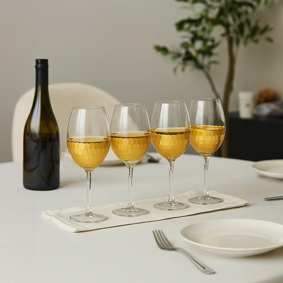 Set of four astrid large wine glasses with hammered gold finish filled with golden liquid on white napkin