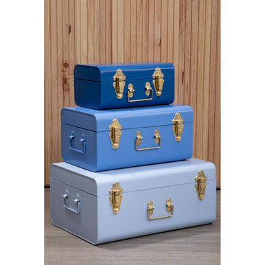 Set of three assorted blue metal storage trunks with gold hardware stacked in vintage suitcase style for stylish storage