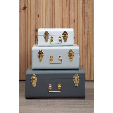 Stacked three assorted grey storage trunks in matte white light blue and dark gray with brass hardware by parley