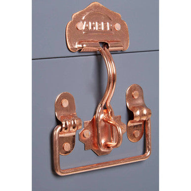 Copper-colored metal latch with ornate arched top and scrollwork on two grey storage trunks parley set