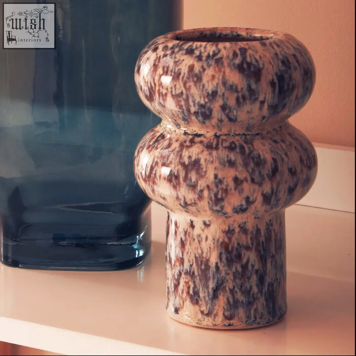A small speckled vase made of ceramic with a brown and beige glaze and two rounded bulbous sections stacked vertically