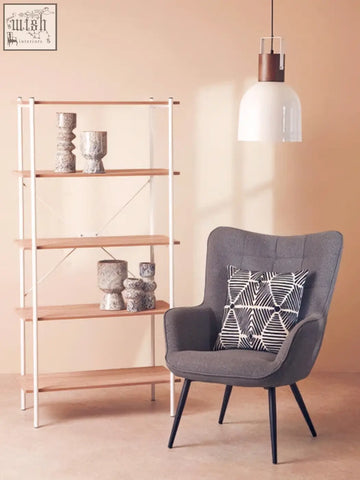Gray upholstered armchair with black legs and a geometric pillow next to a small speckled vase on a side table
