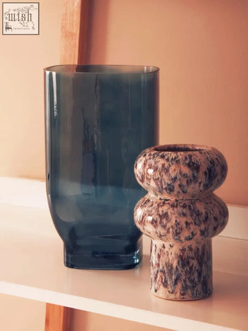 A sleek dark blue glass vase stands beside a small speckled vase ceramic planter with earthy stacked rounded forms
