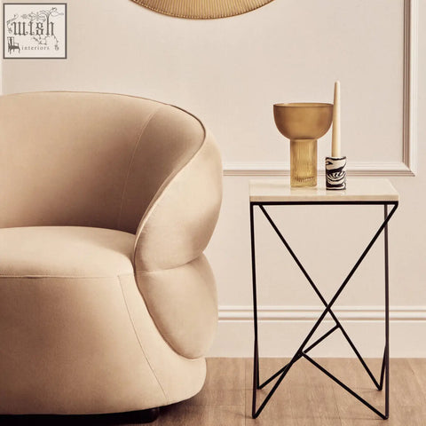 Cream-colored velvet armchair next to shalimar marble top square side table with black iron base