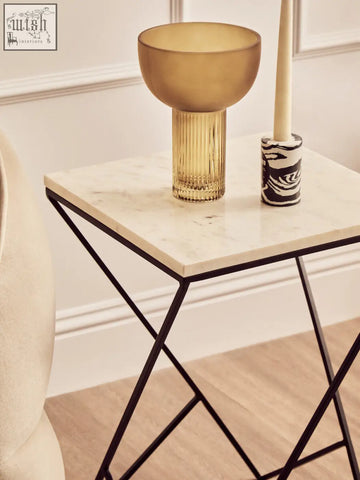 Golden ribbed glass bowl with rounded rim and amber hue on shalimar marble top square side table with black iron base