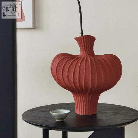 A shaped ceramic vase in terracotta red with vertical ridges and a flared neck holding a dark branch