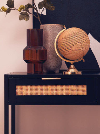 A woven rattan globe with brass stand and metallic rim displayed on the sherman black wood rattan two drawer console table