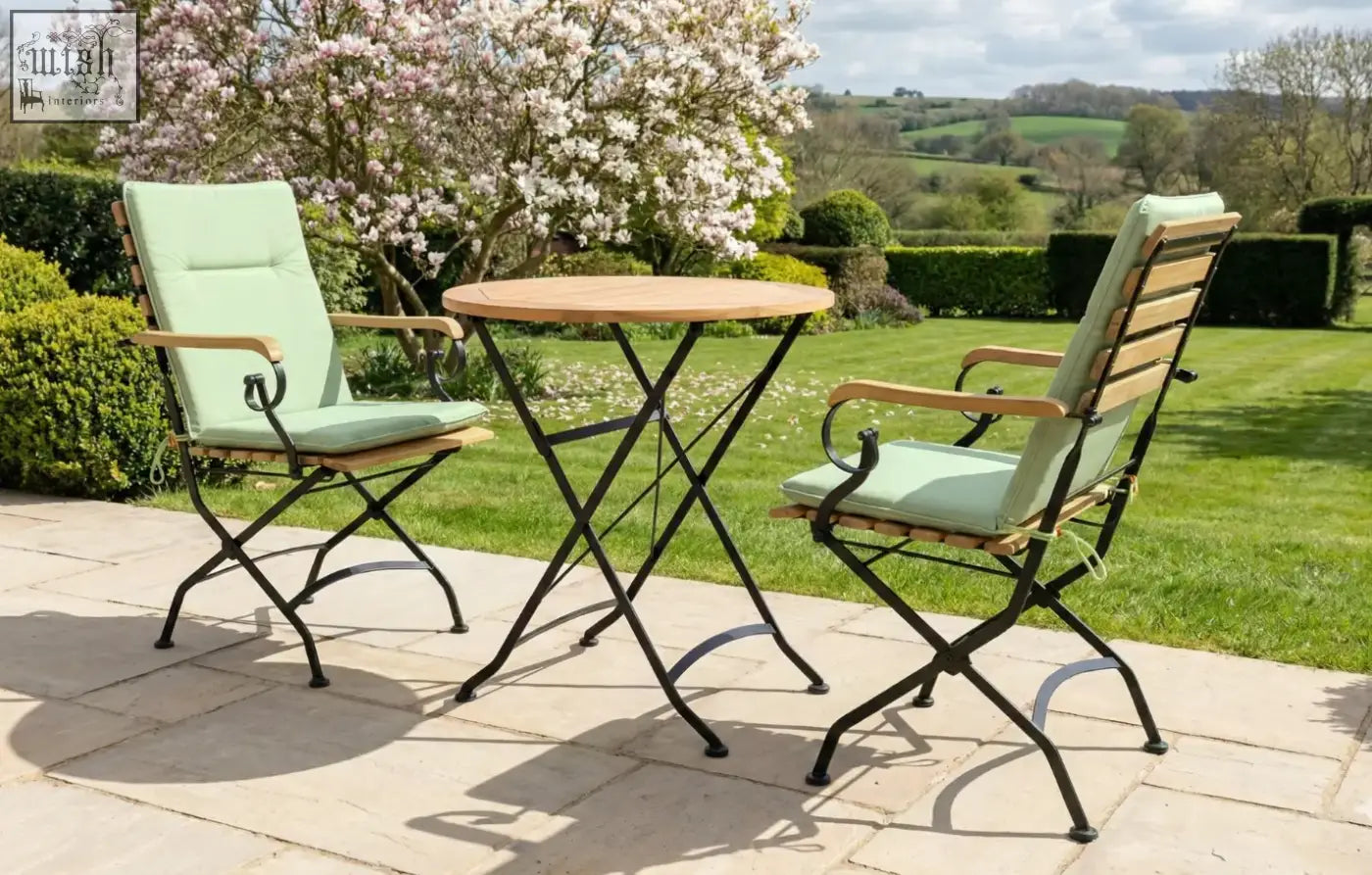 Light green cushioned folding chairs with wooden armrests in a Sicily 2 seater grade ab teak garden dining set