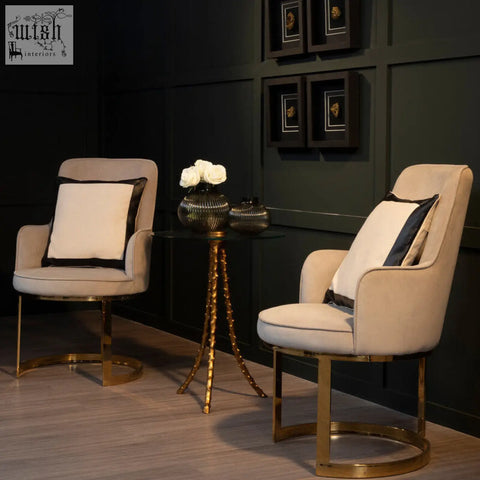 Beige upholstered armchairs with warm gold triple-leg base and black-trimmed pillows near sika large side table