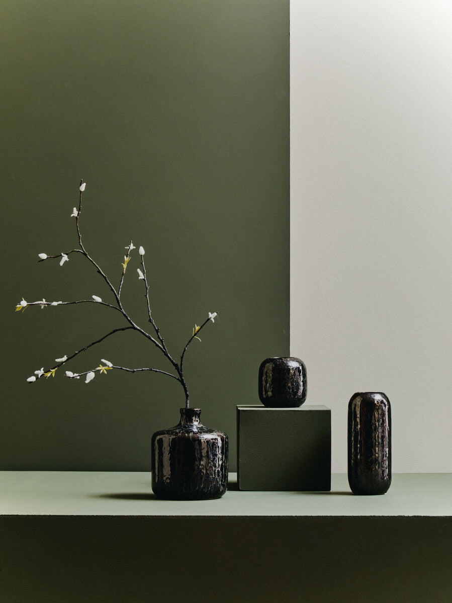 Silas dark blue bottle vase is a sleek glossy ceramic dark blue vase with a rounded body holding white blossoms