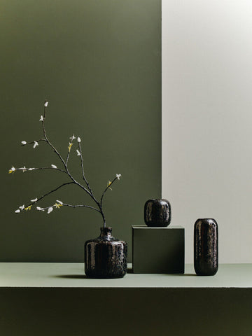 A sleek glossy dark blue ceramic planter with a rounded body holds delicate white blossoms on slender branches
