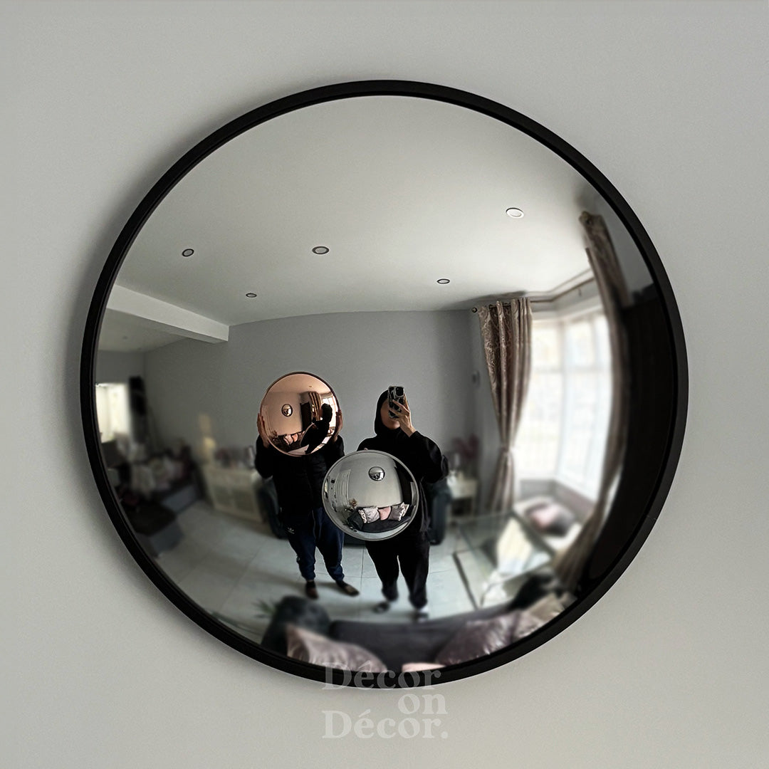 Black framed silver bubble interactive mirror with convex reflective surface showing two people indoors