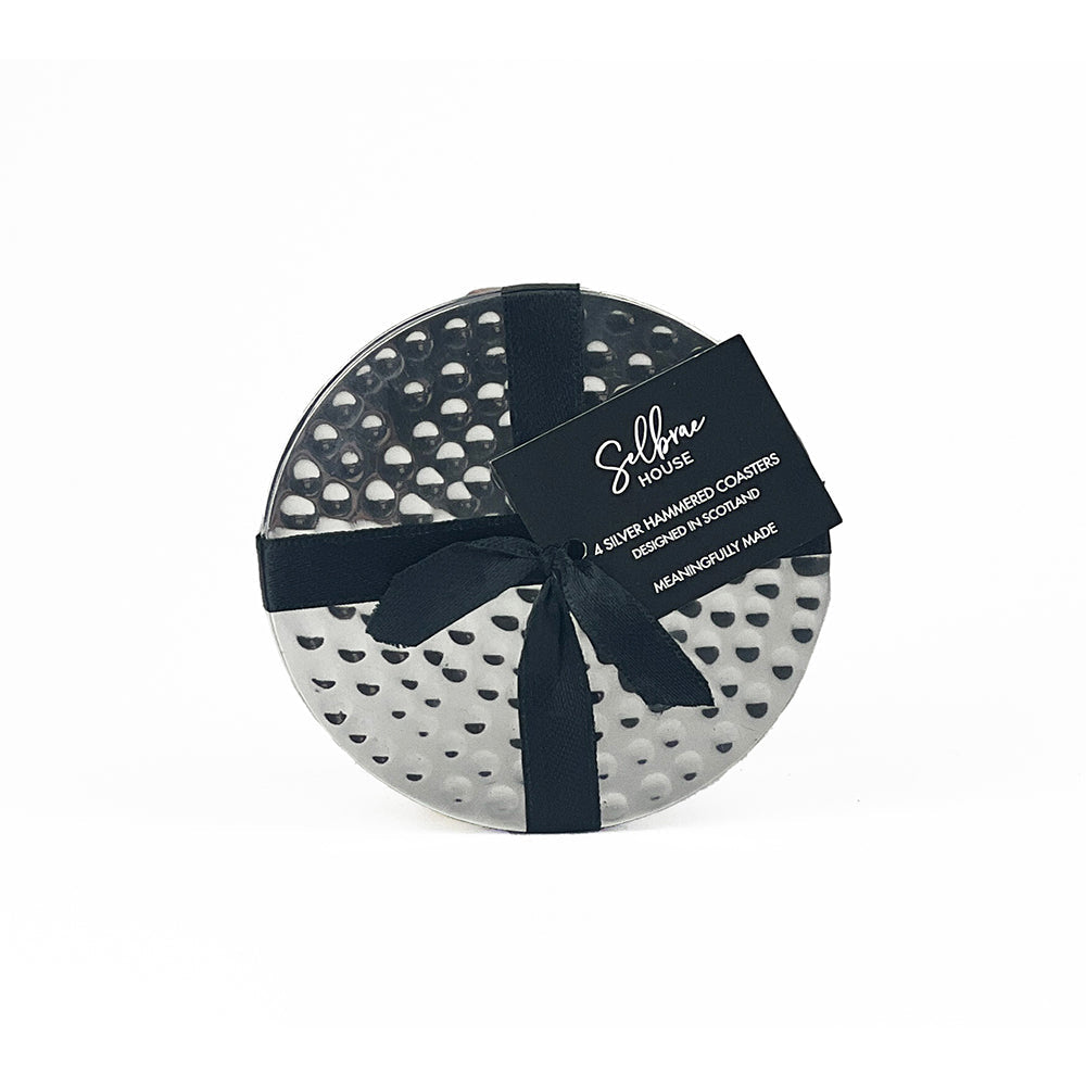 Set of four silver flat hammered coasters in a circular gift box with black ribbon labeled selbma house