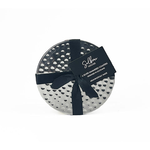 Set of four silver flat hammered coasters in a circular gift box with black ribbon labeled selbma house