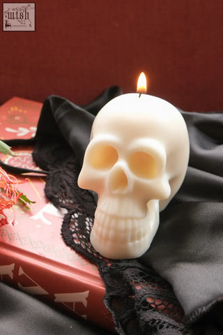 A white wax skull candle with a lit wick perfect for spooky or decorative use