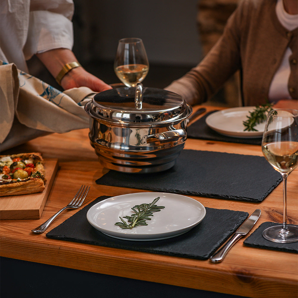 Shiny stainless steel multi tiered serving pot with lid and handle shown on large place mats slate trivets set of 2