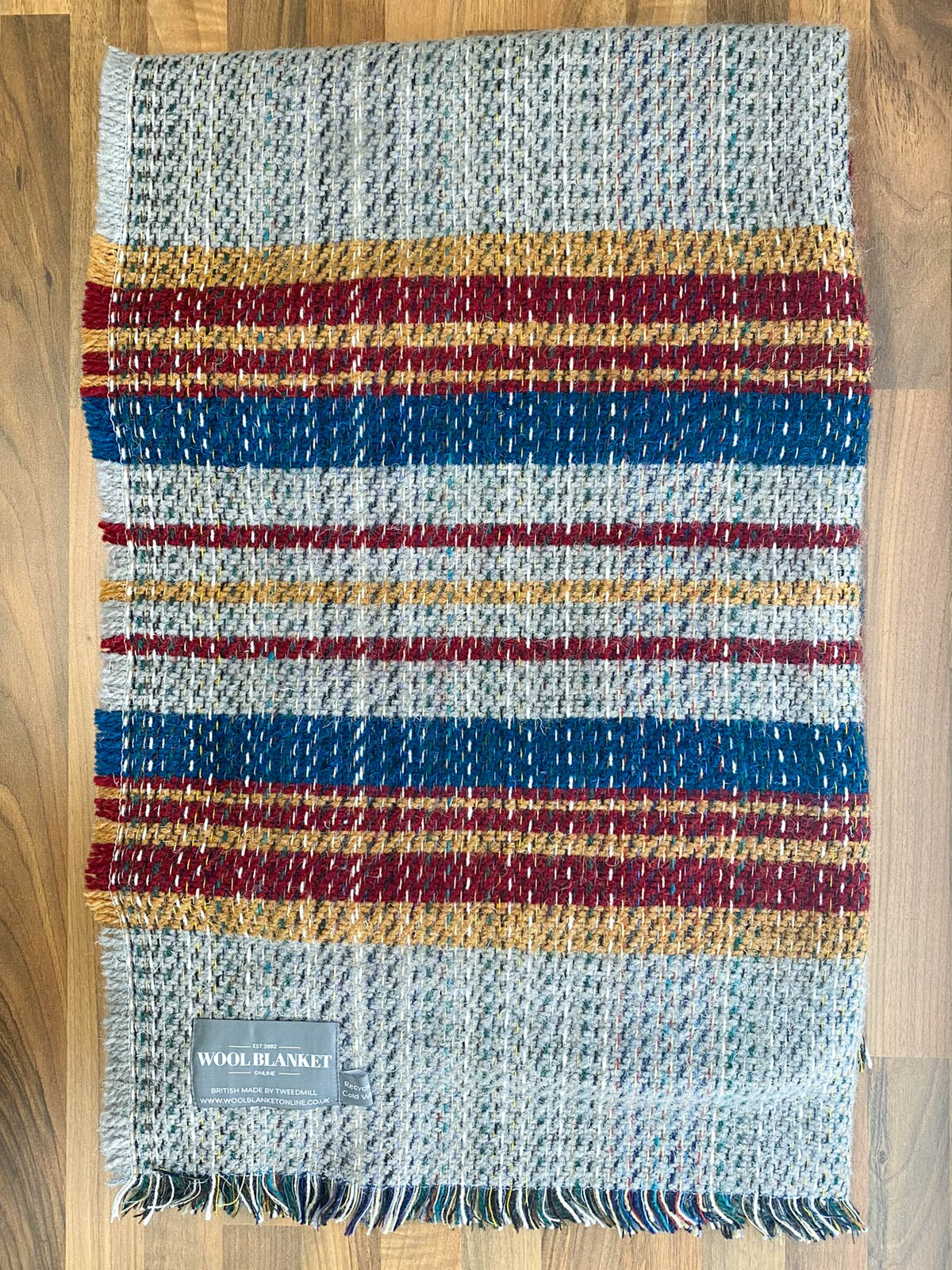 A cozy small checked random recycled wool blanket with horizontal gray red blue and mustard stripes and fringed edges