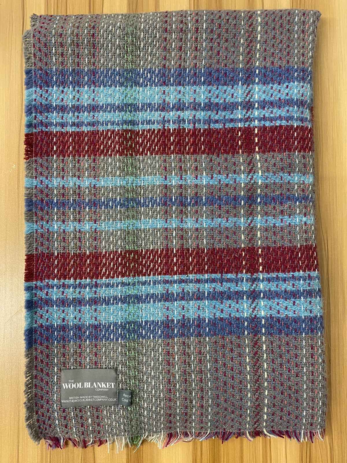 A cozy small checked random recycled wool blanket with a rich gray blue red and green plaid and frayed edges