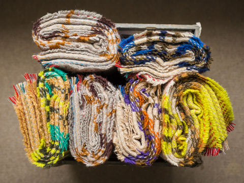 A collection of colorful small checked random recycled wool blankets with textured patterns and frayed edges