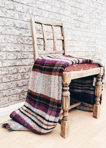 A rustic wooden chair with a cozy small checked random recycled wool blanket in purple maroon black and beige stripes