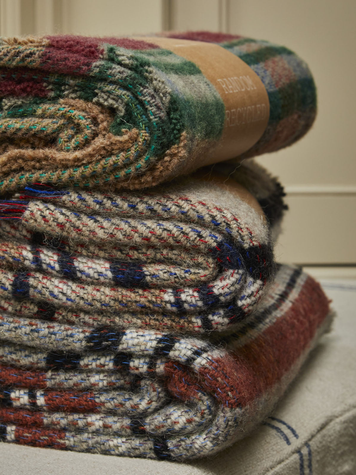 Stack of three small checked random recycled wool blankets in earthy tones with brown paper band on top