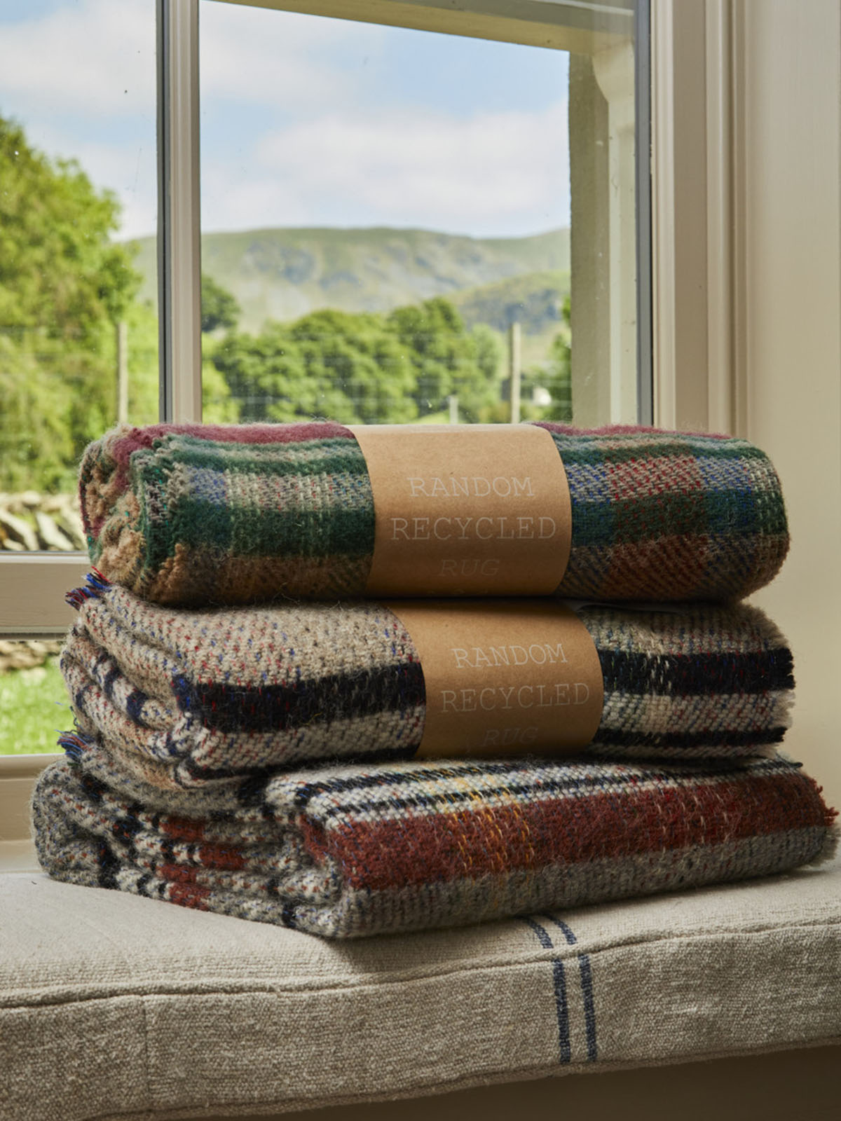 Stack of three folded small checked random recycled wool blankets with earthy tones and tan paper bands