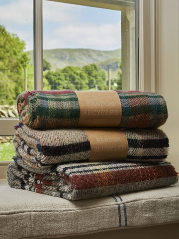 Stack of three folded small checked random recycled wool blankets with earthy tones and tan paper bands