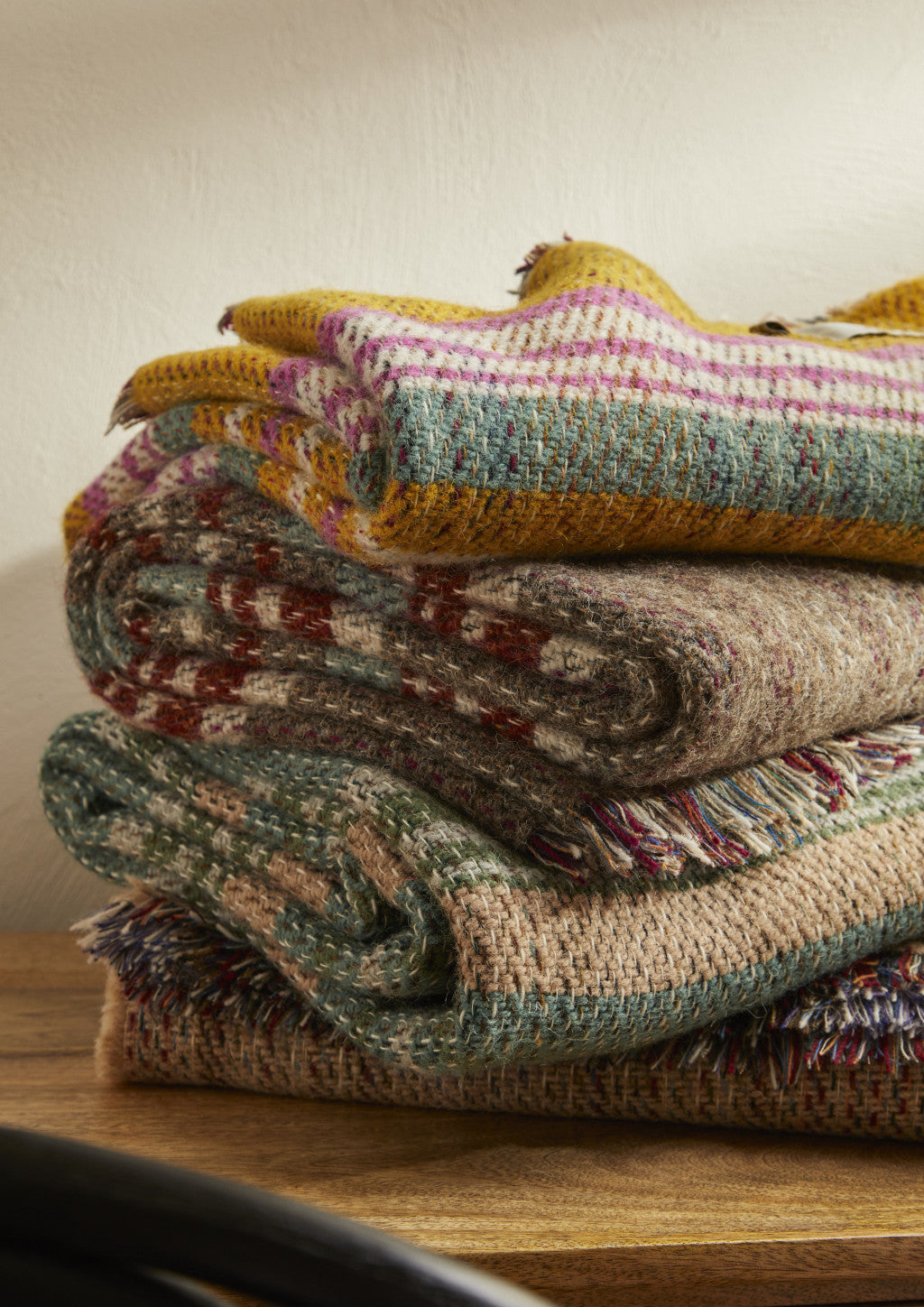 Stack of cozy small checked random recycled wool blankets in earthy tones with colorful stripes