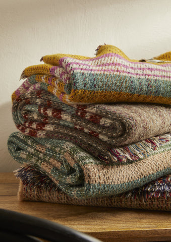 Stack of cozy small checked random recycled wool blankets in earthy tones with colorful stripes