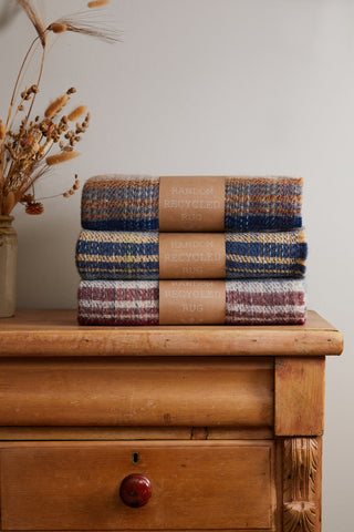 Stack of three small checked random recycled wool blankets with striped patterns in blue beige and burgundy tones